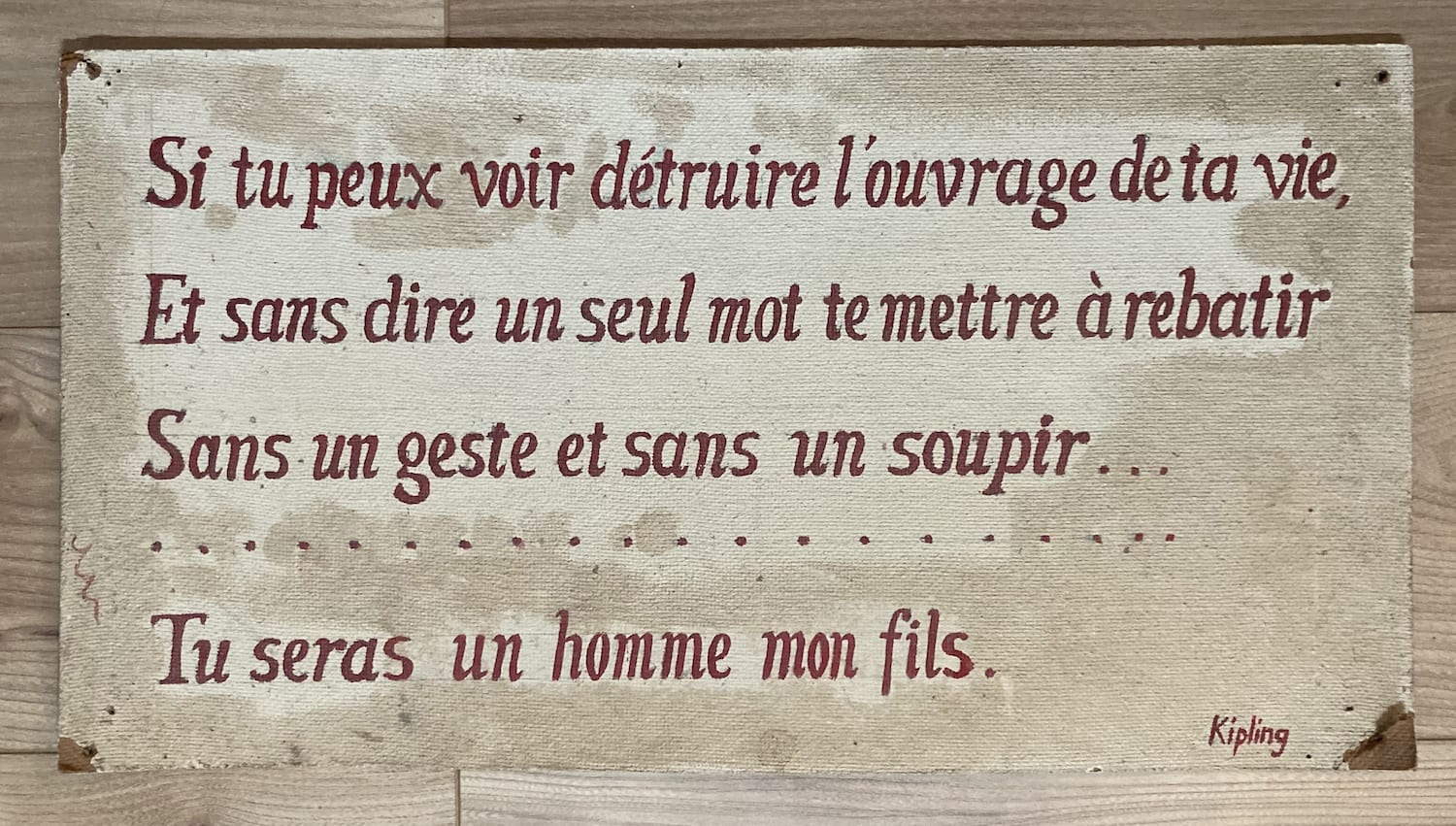 A hardboard pannel with handwritten text in red. It has lines from the poem below in French.